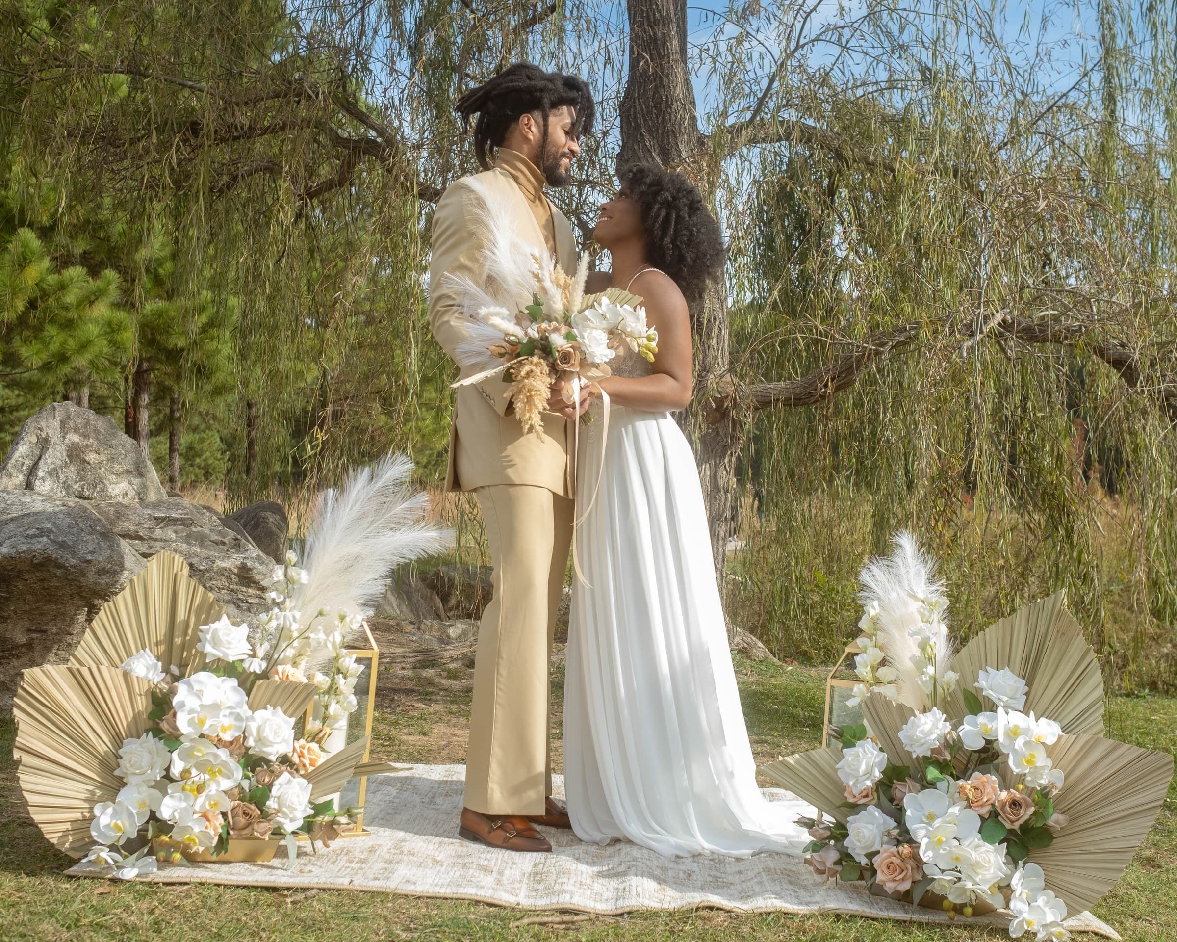 Couple holding a bouquet and gazing at each other beneath a willow tree