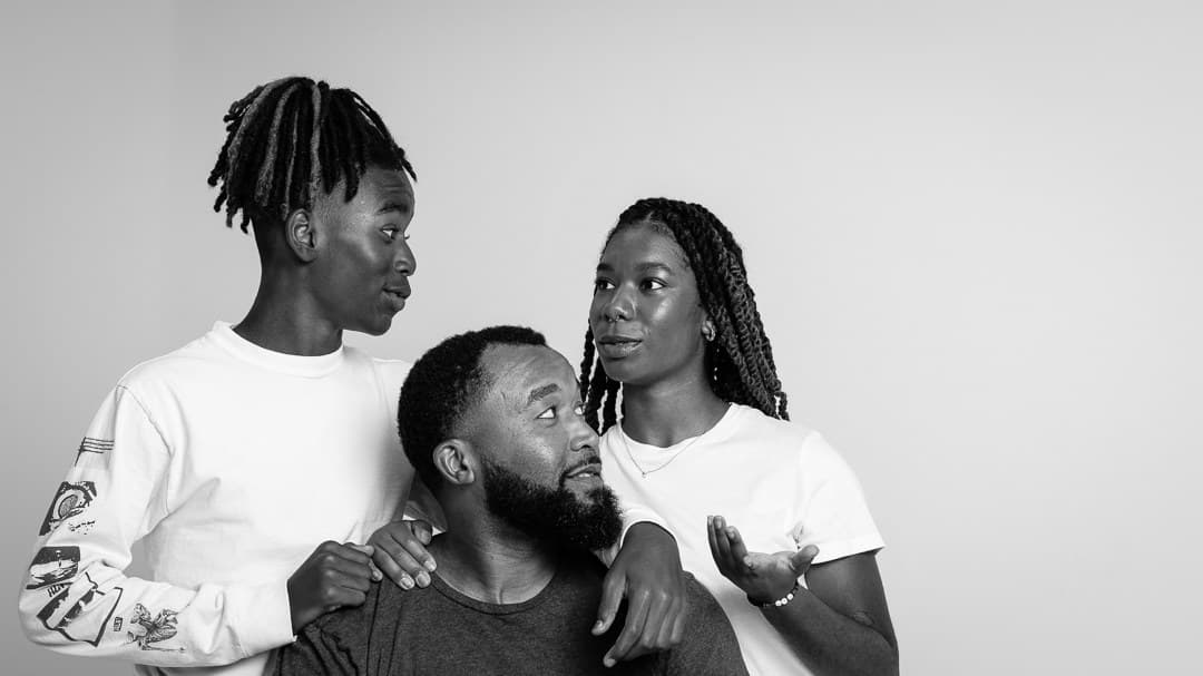 Black and white studio portrait of a father looking up at his teenage son and daughter