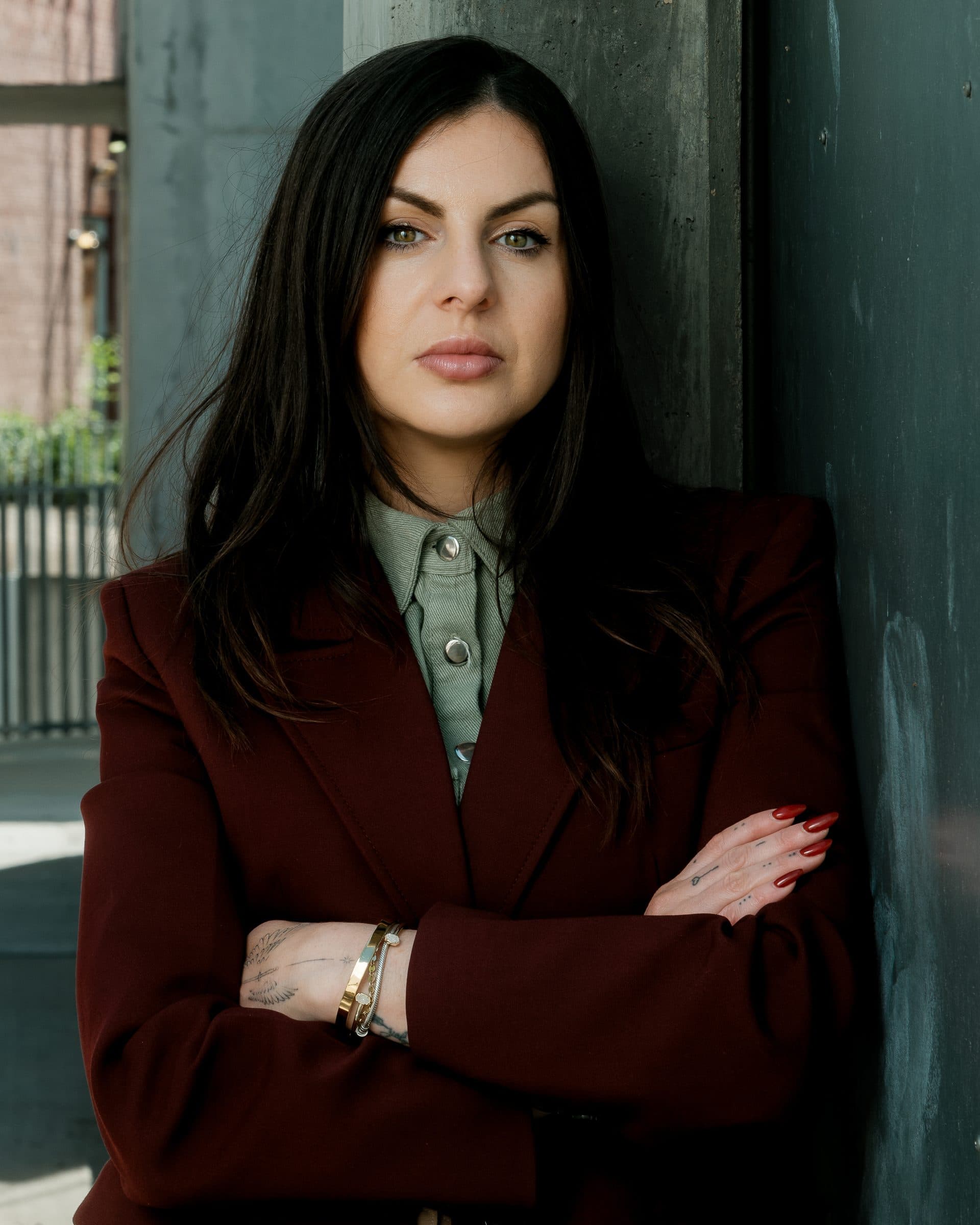 Branding portrait: woman in dark red blazer leaning against a teal door, outdoor editorial headshot
