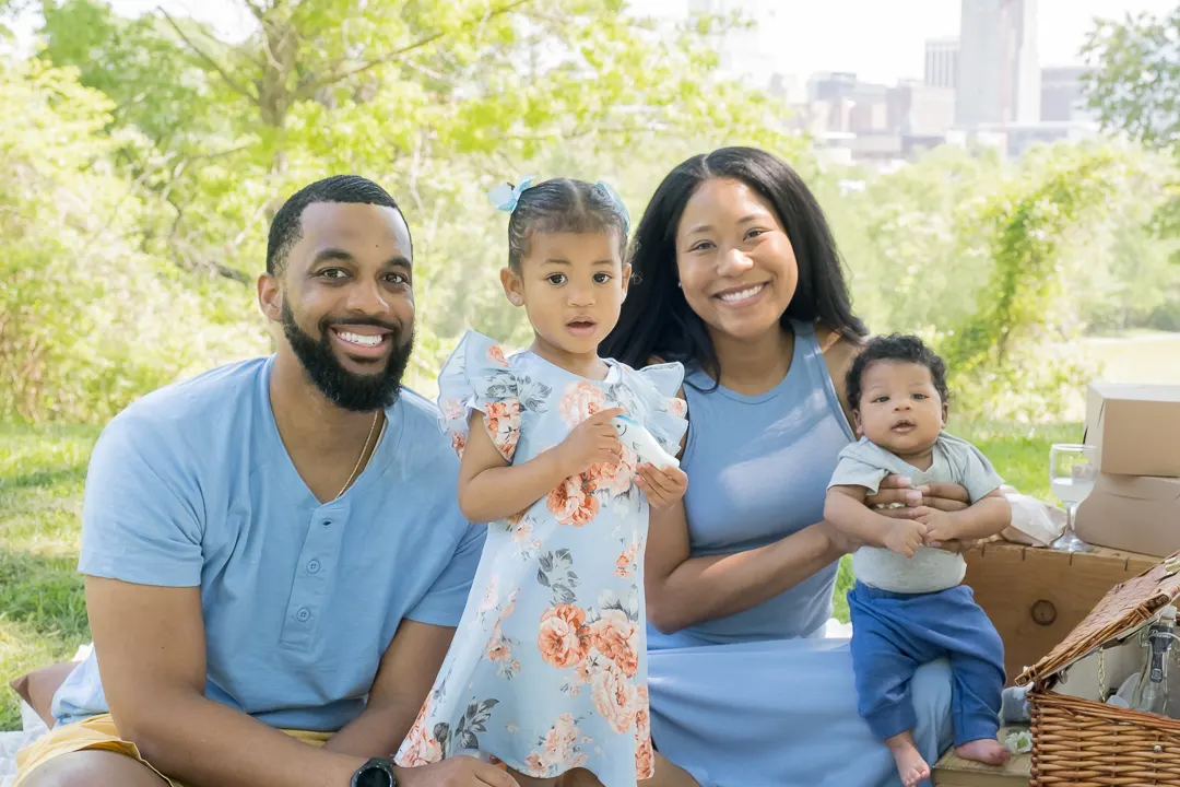 Black family of four having a picnic on the grass with the downtown Raleigh skyline behind them during a spring session
