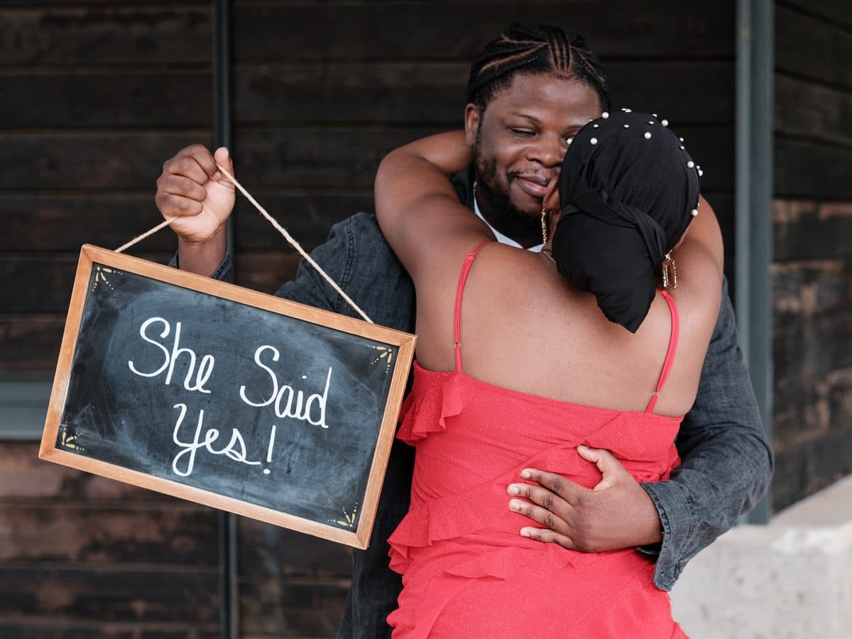 Couple hugging while holding a She Said Yes sign