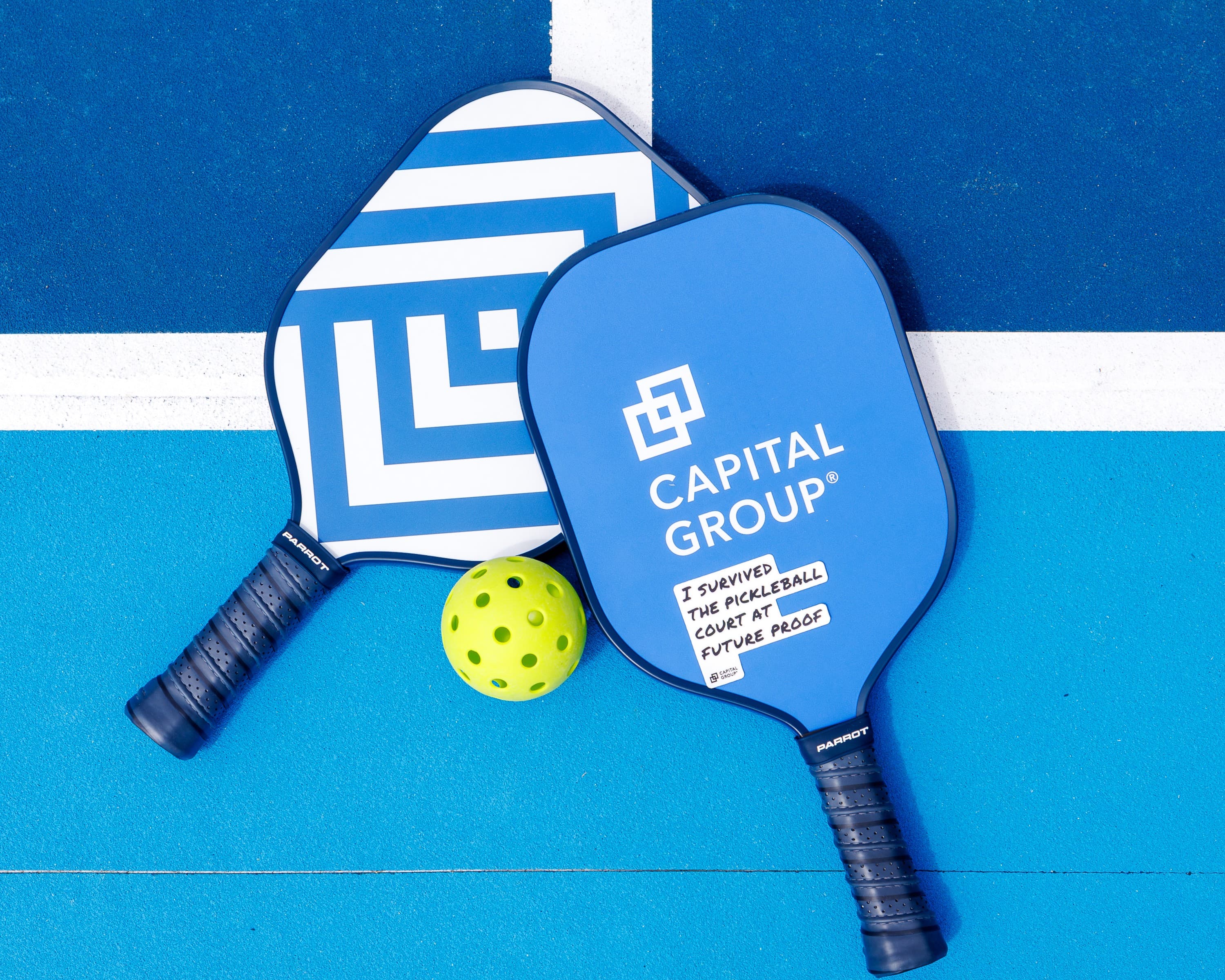 Two blue branded pickleball paddles and a yellow ball laid on a blue court at a corporate event