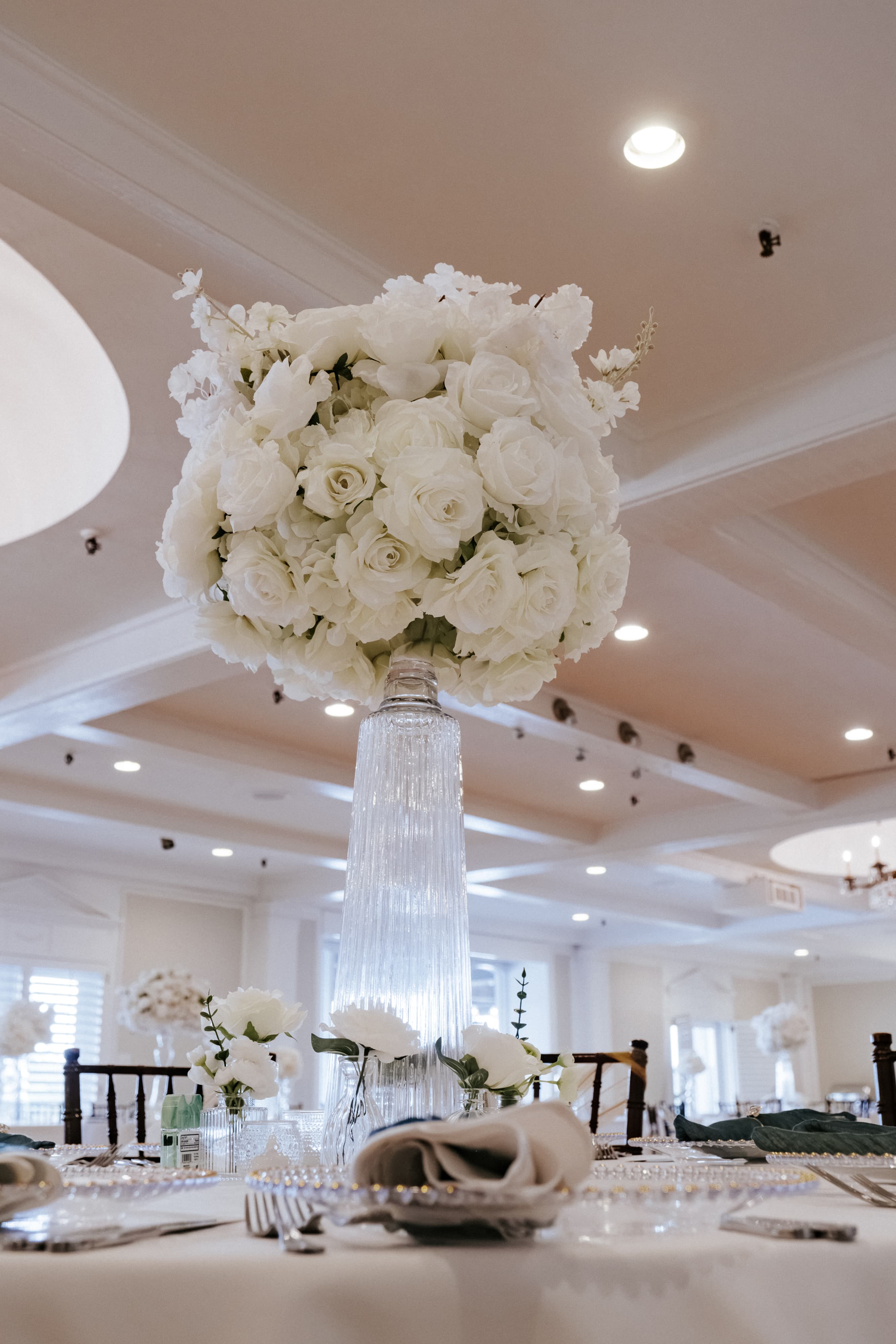 Tall white rose centerpiece in a crystal vase on a wedding reception table