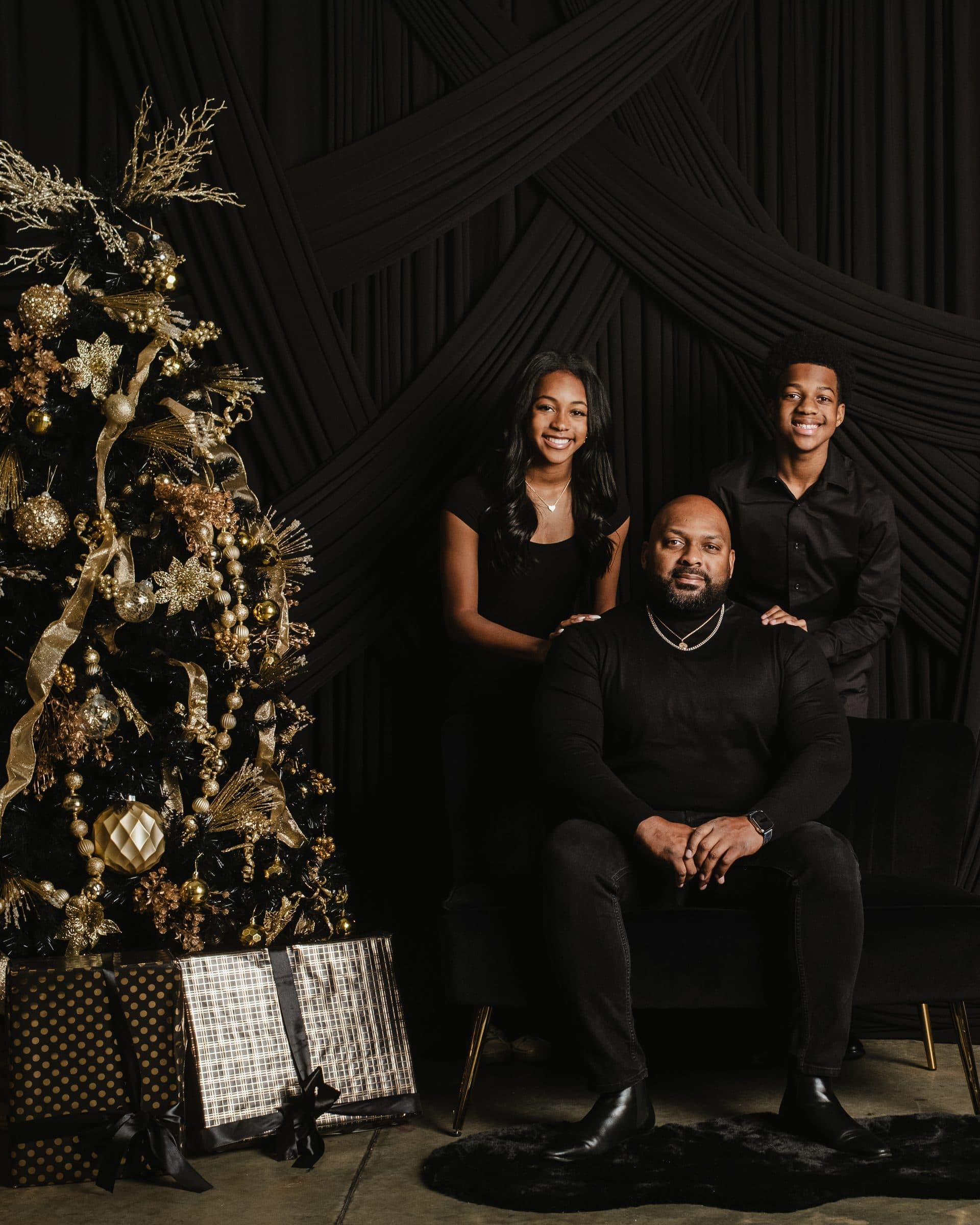 Black father and two children posing together beside a decorated Christmas tree