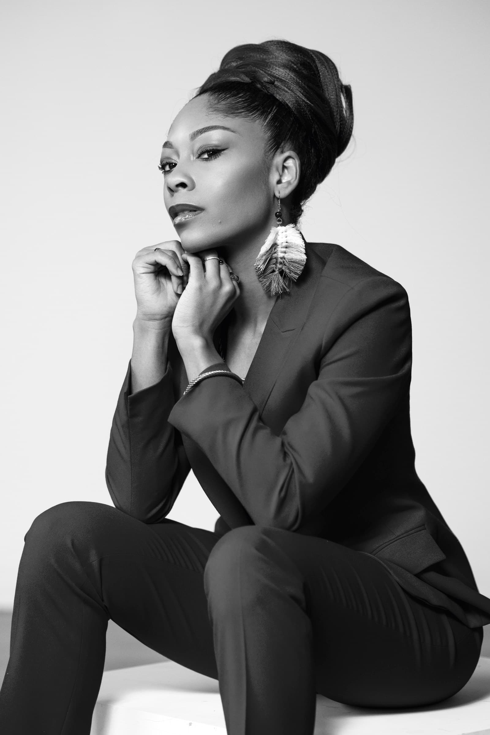 Black and white editorial portrait of a woman in a dark suit resting her chin on her hands