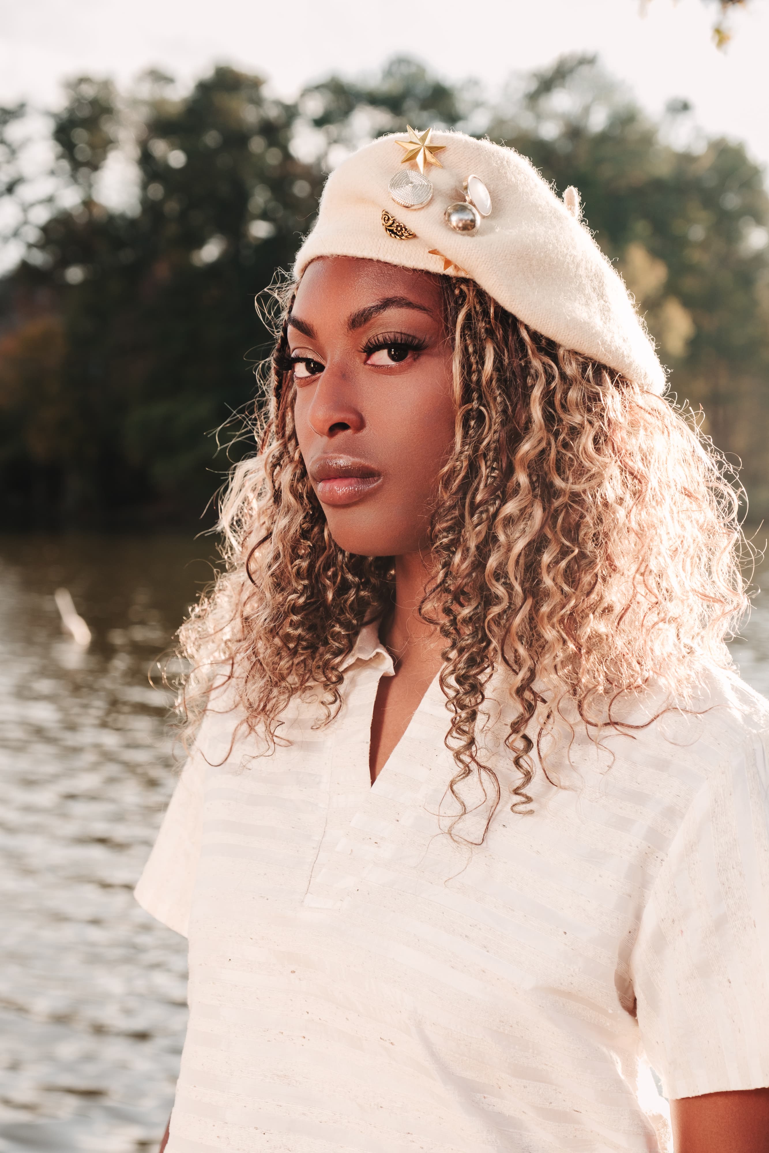 Woman in a cream beret posing beside a lake